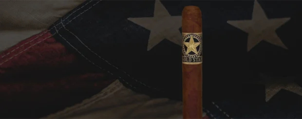 Gold Star cigar featuring a bold gold star emblem on a black band, positioned in front of a rustic American flag backdrop, symbolizing honor, heritage, and craftsmanship.