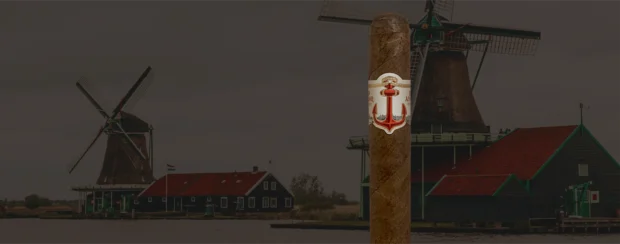 Red Anchor cigar with a nautical-inspired red anchor band design, standing before a scenic Dutch landscape featuring historic windmills and waterfront cottages, symbolizing heritage and craftsmanship.