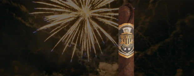 Firecracker Maduro cigar with bold band design featuring an eagle and shield, set against a backdrop of golden fireworks in the night sky.